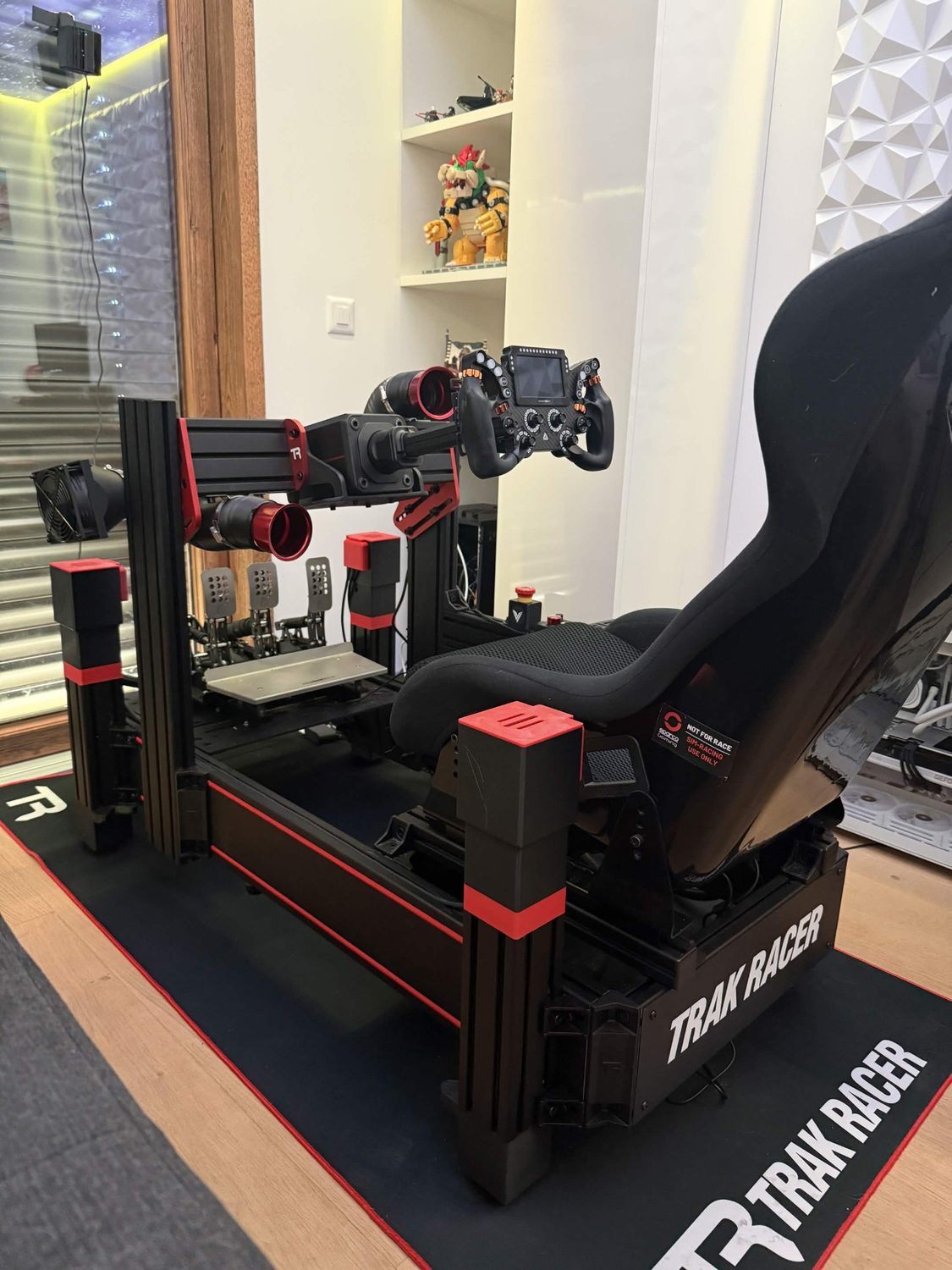 Cockpit de sim racing complet porté par des vérins V-TRAX aux embouts rouges : volant, pédalier, siège baquet et ventilateurs