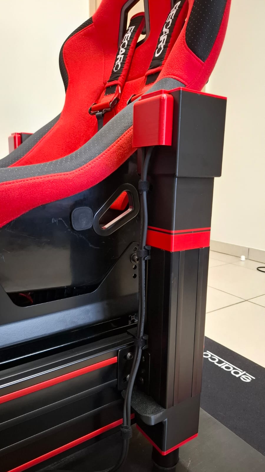 Fixation d'un vérin V-TRAX sous un siège baquet Recaro, avec passage de câble le long de la colonne